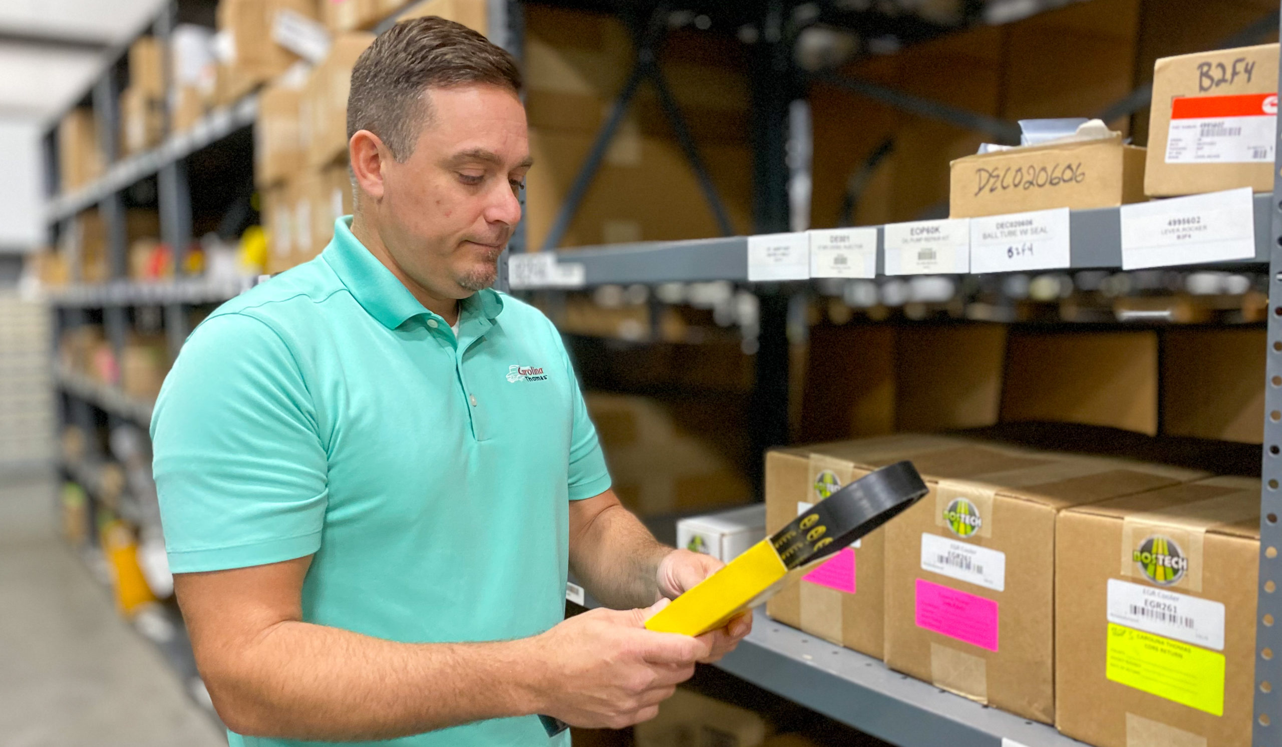 Man in a warehouse looking at a bus engine belt part